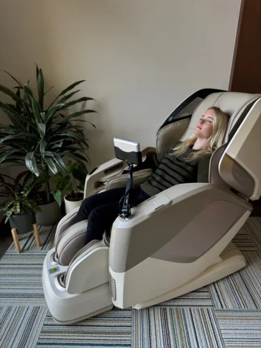 Woman relaxing in a beige massage chair in a cozy room with plants.