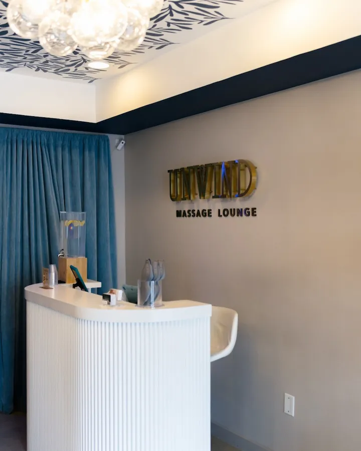 Reception area of Untamed Massage Lounge with a sleek white desk and blue curtains.