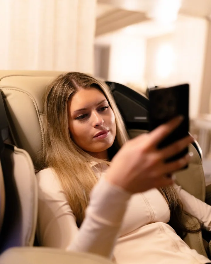 Young woman taking a selfie while relaxing on a beige chair.